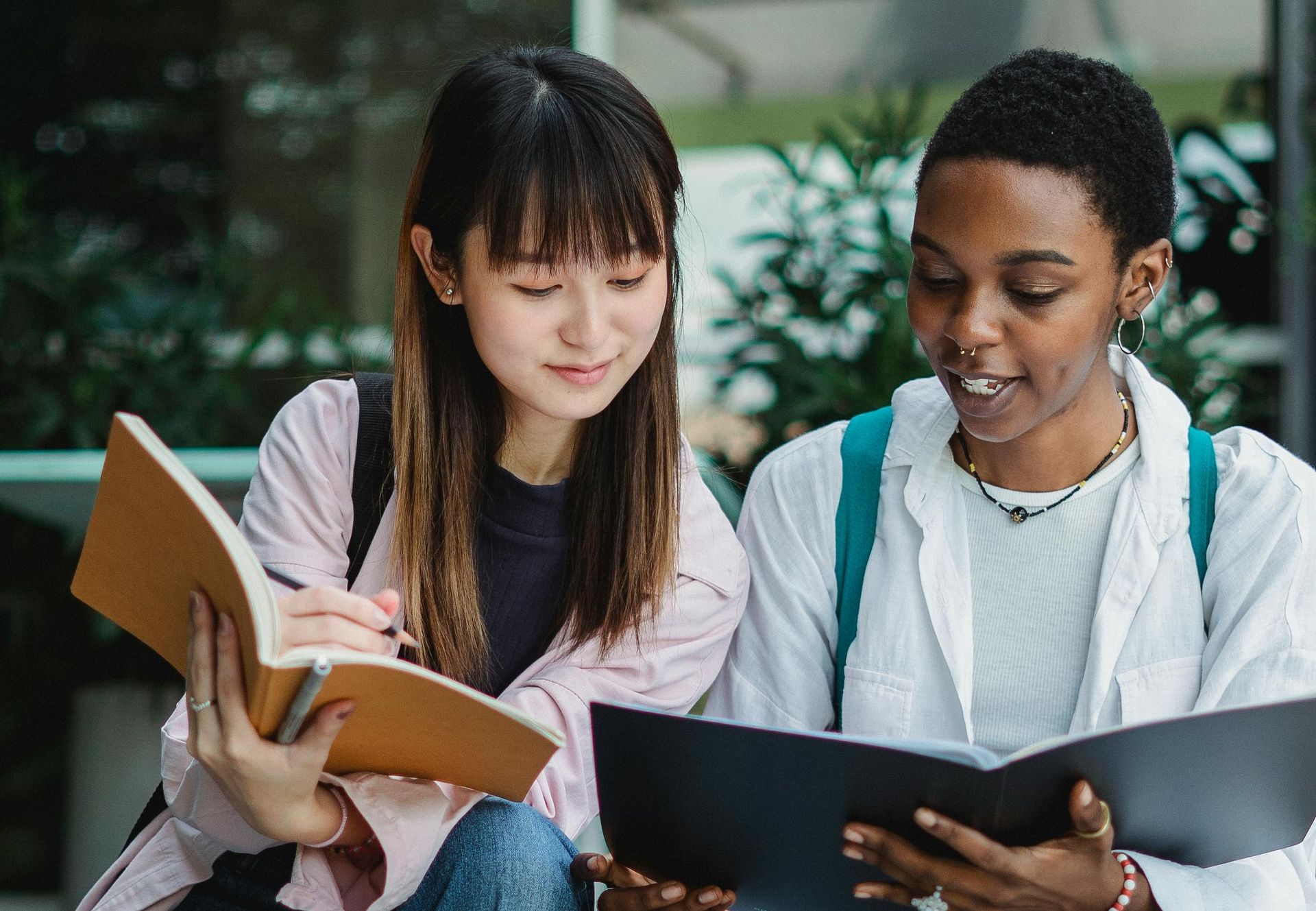 two  woman are sitting next to each other reading books.