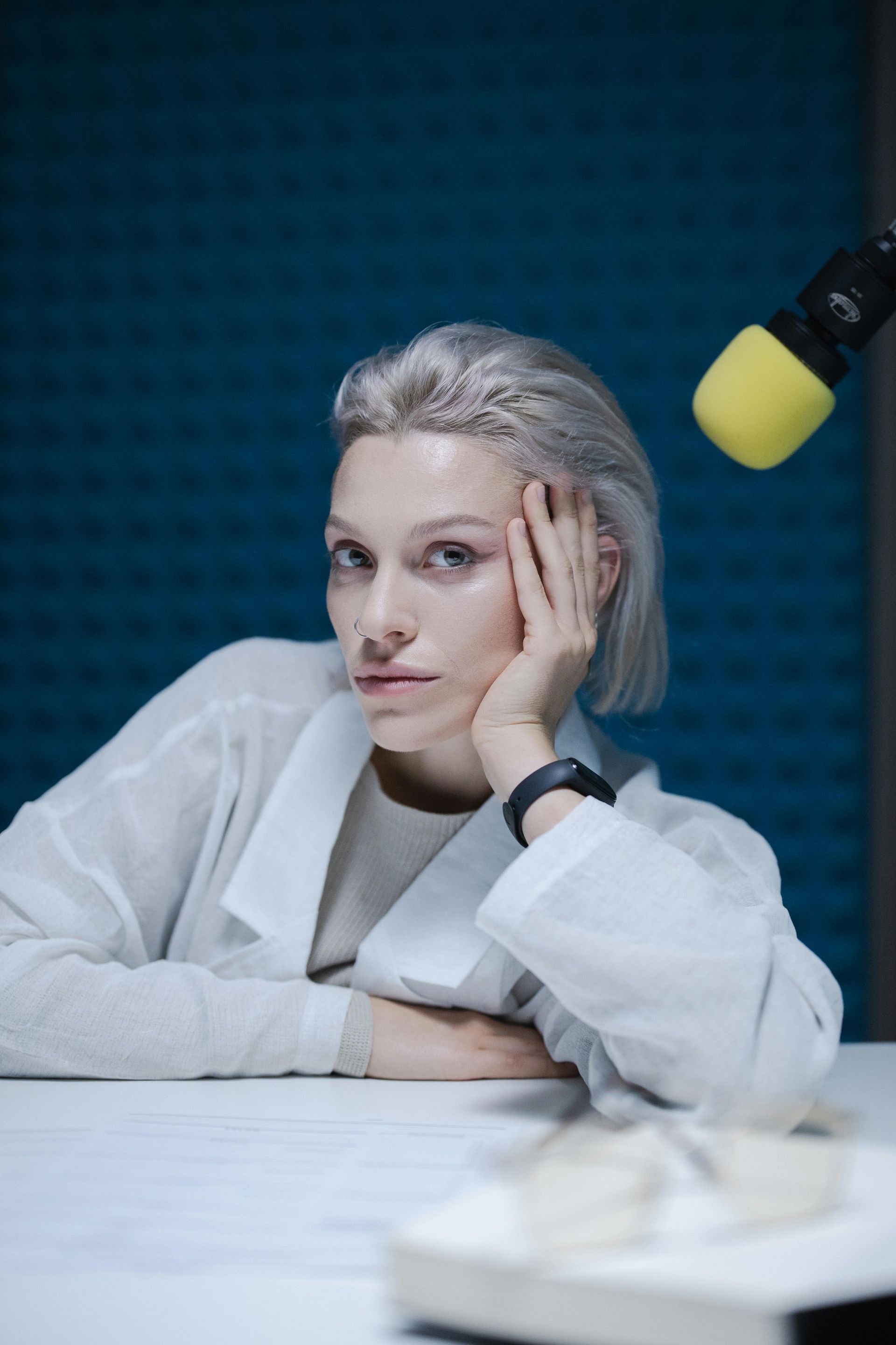 A woman is sitting at a table with her hand on her face in front of a microphone.