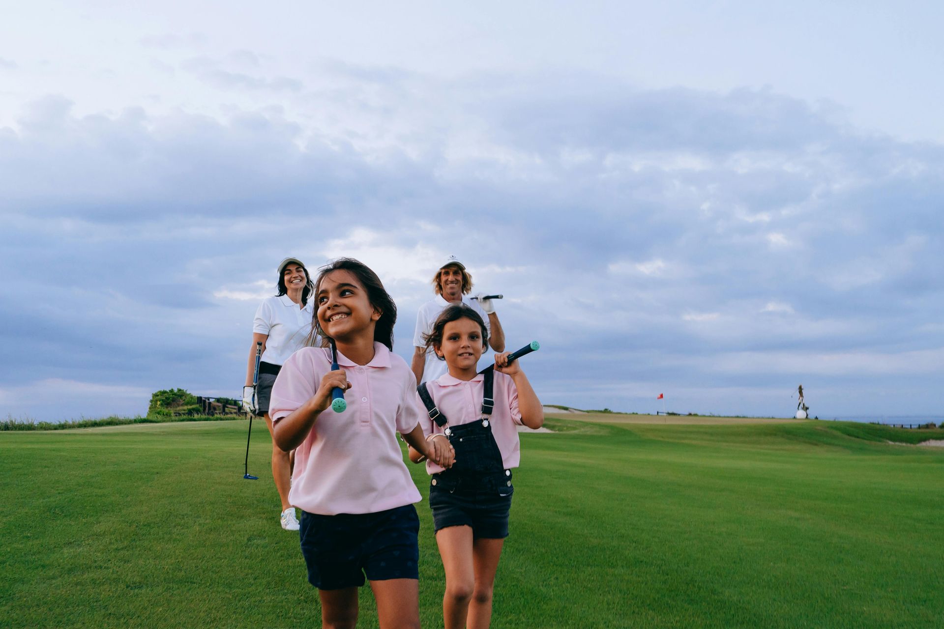 A group of young girls are walking on a golf course holding golf clubs.