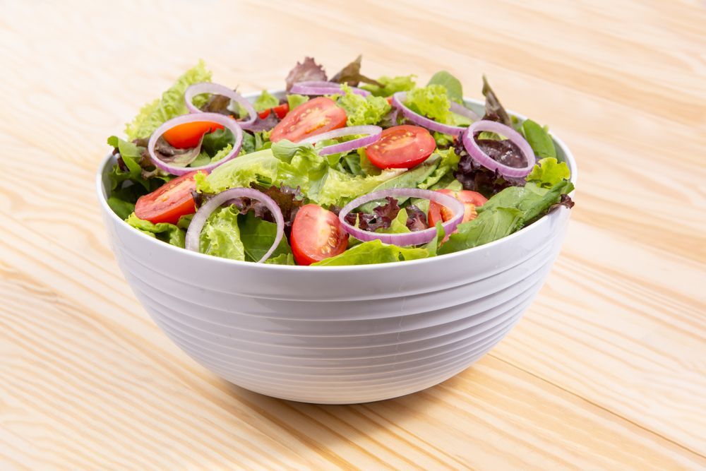 Salad in A White Bowl on A Wooden Surface with Red Onions — Mount Louisa Snack Bar in Mount Louisa, QLD