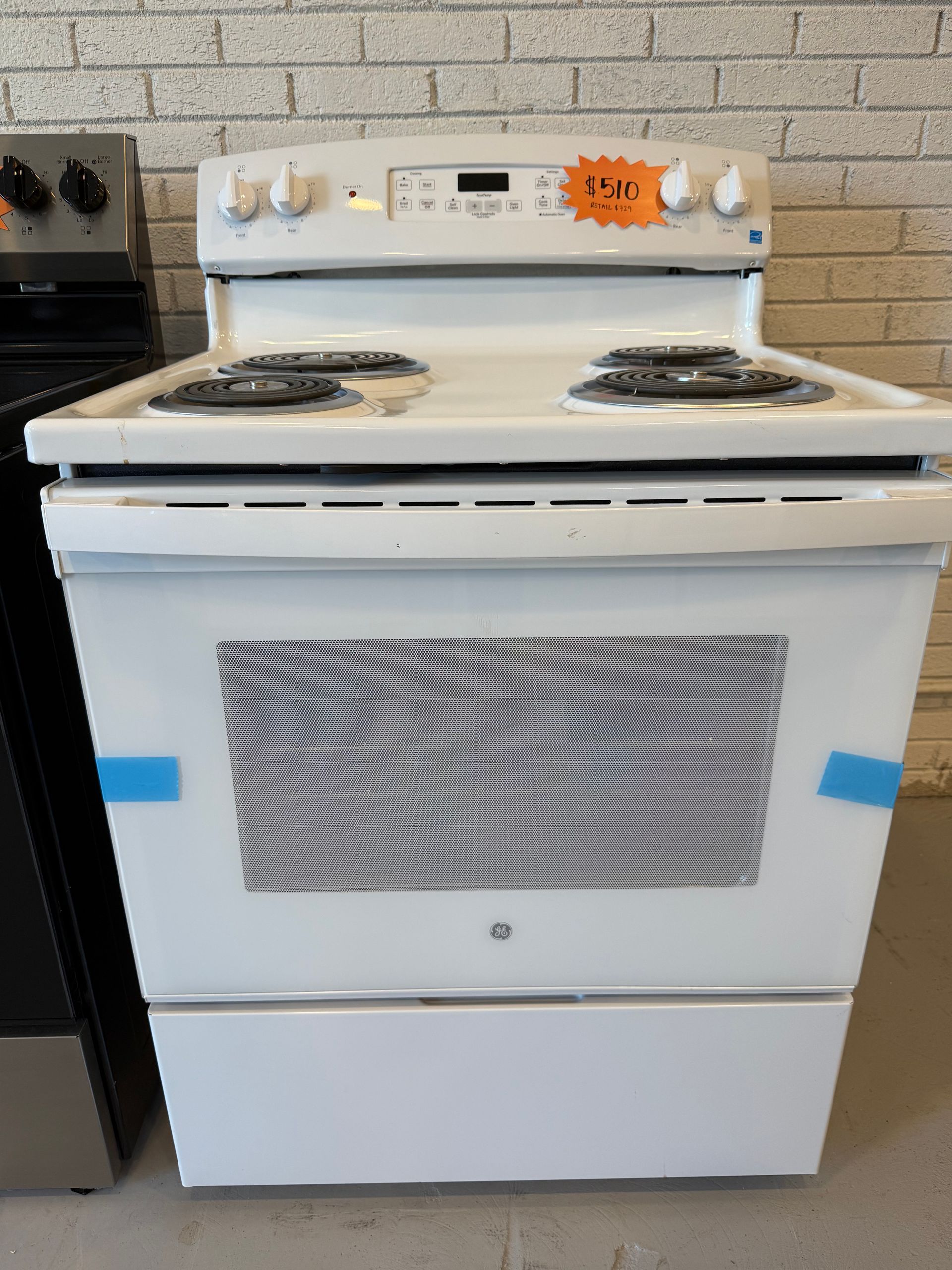 A white stove with a price tag on it is sitting in front of a brick wall.