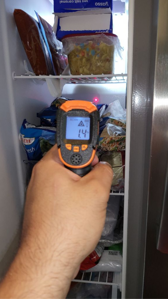A person is holding a thermometer in front of a refrigerator.