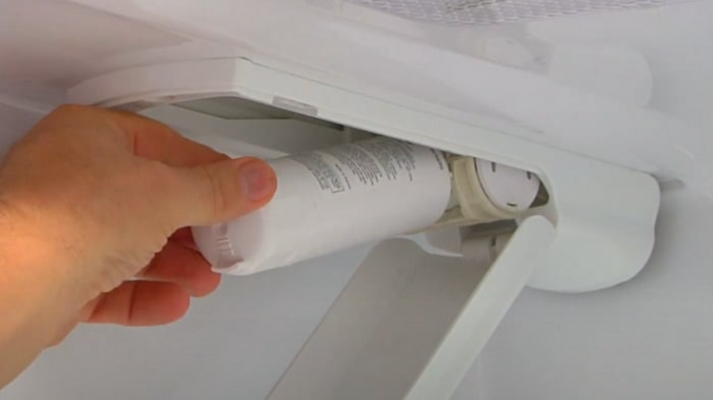 A person is removing a water filter from a refrigerator.