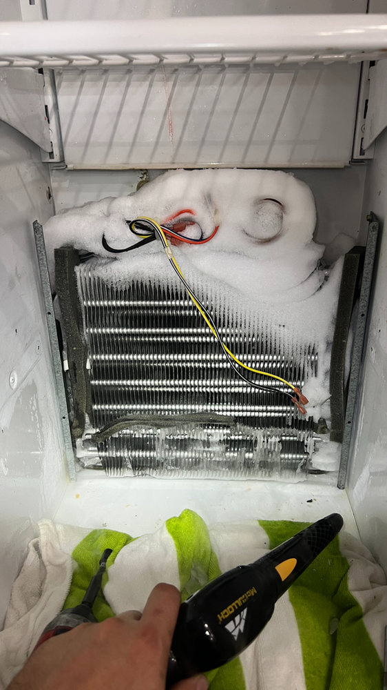 A person is cleaning the inside of a refrigerator with a vacuum cleaner.