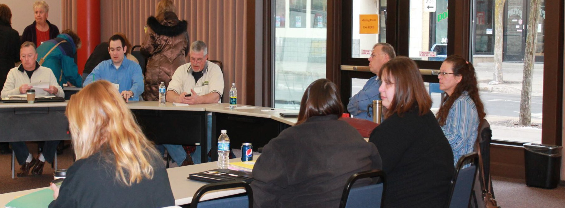 Group of adults seated around tables participating in a meeting or training session.
