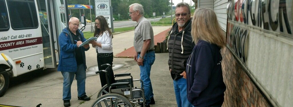Group of people standing near a transit vehicle, with a wheelchair in the foreground.