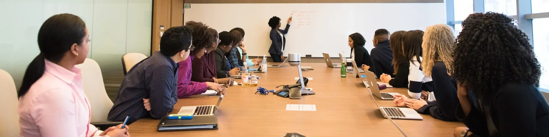 Group of people in a meeting as a presenter writes on a whiteboard.