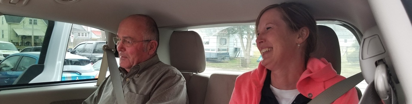 two passengers seated in the back of a vehicle wearing seatbelts.