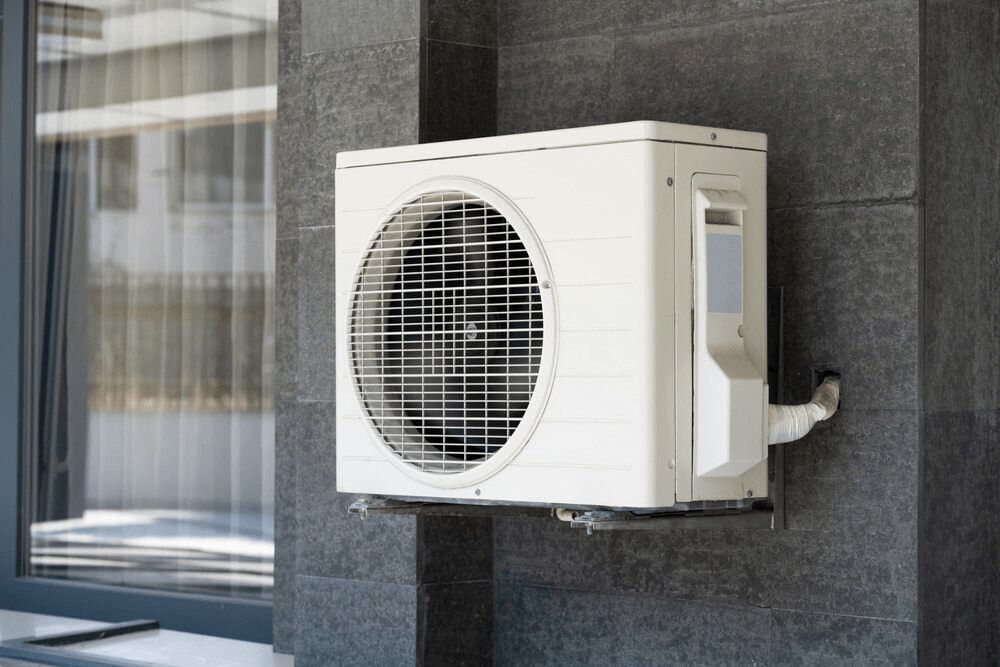 White Air Conditioner is Mounted on the Side of a Building Next to a Window — First Point Air Conditioning in Fyshwick, ACT