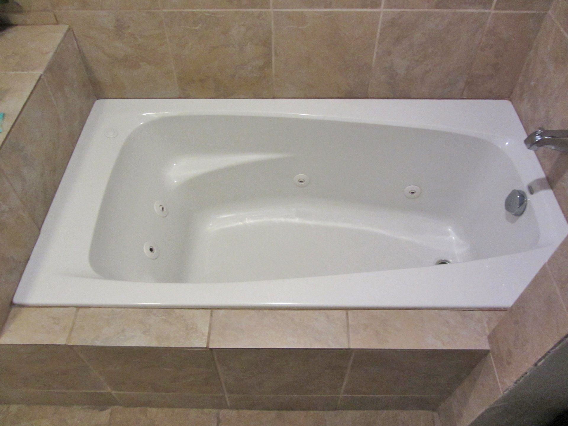 A white bathtub is sitting in a bathroom next to a tiled wall.