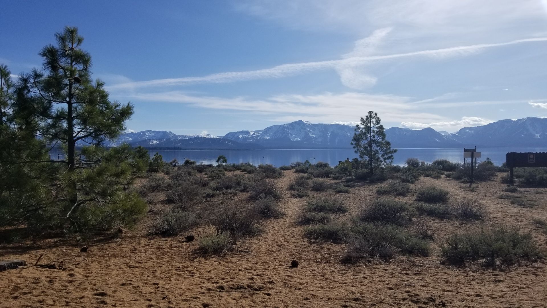 A dirt field with a lake in the background and mountains in the background.