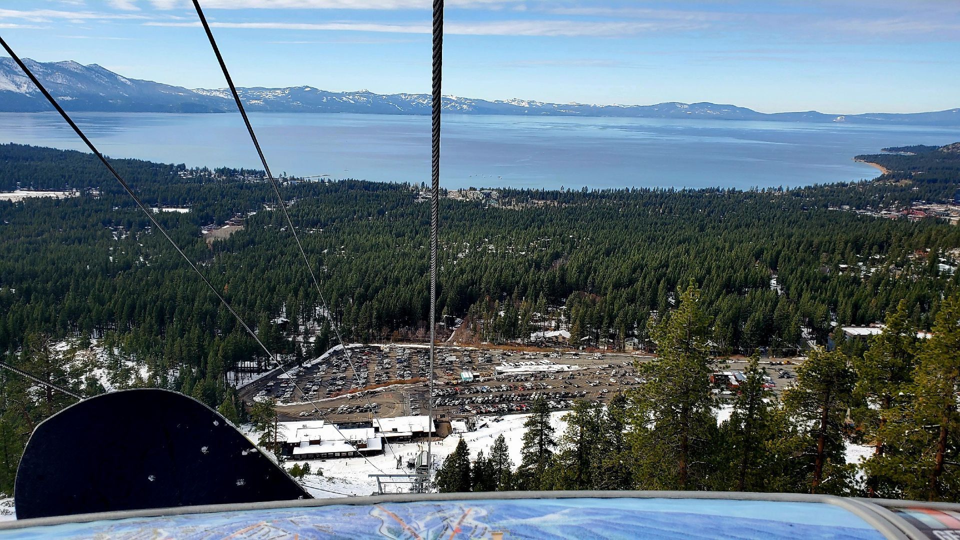 A person is riding a ski lift with a view of a lake and mountains.