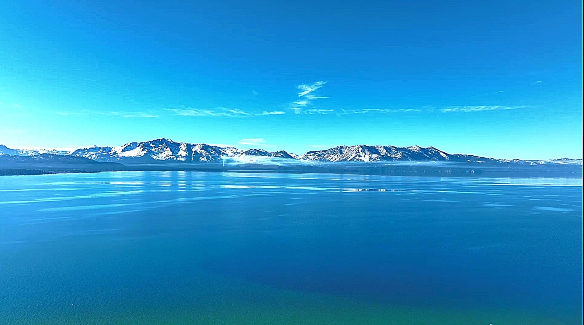 A large body of water with mountains in the background and a blue sky.