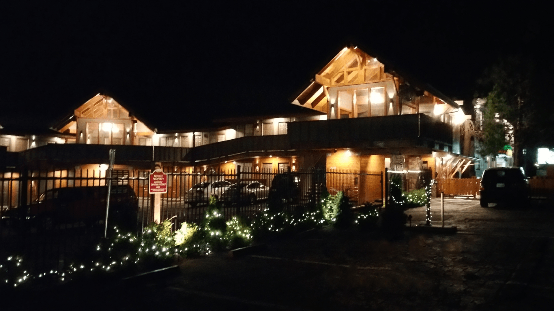 A large building with security gating is lit up at night with cars parked in front of it