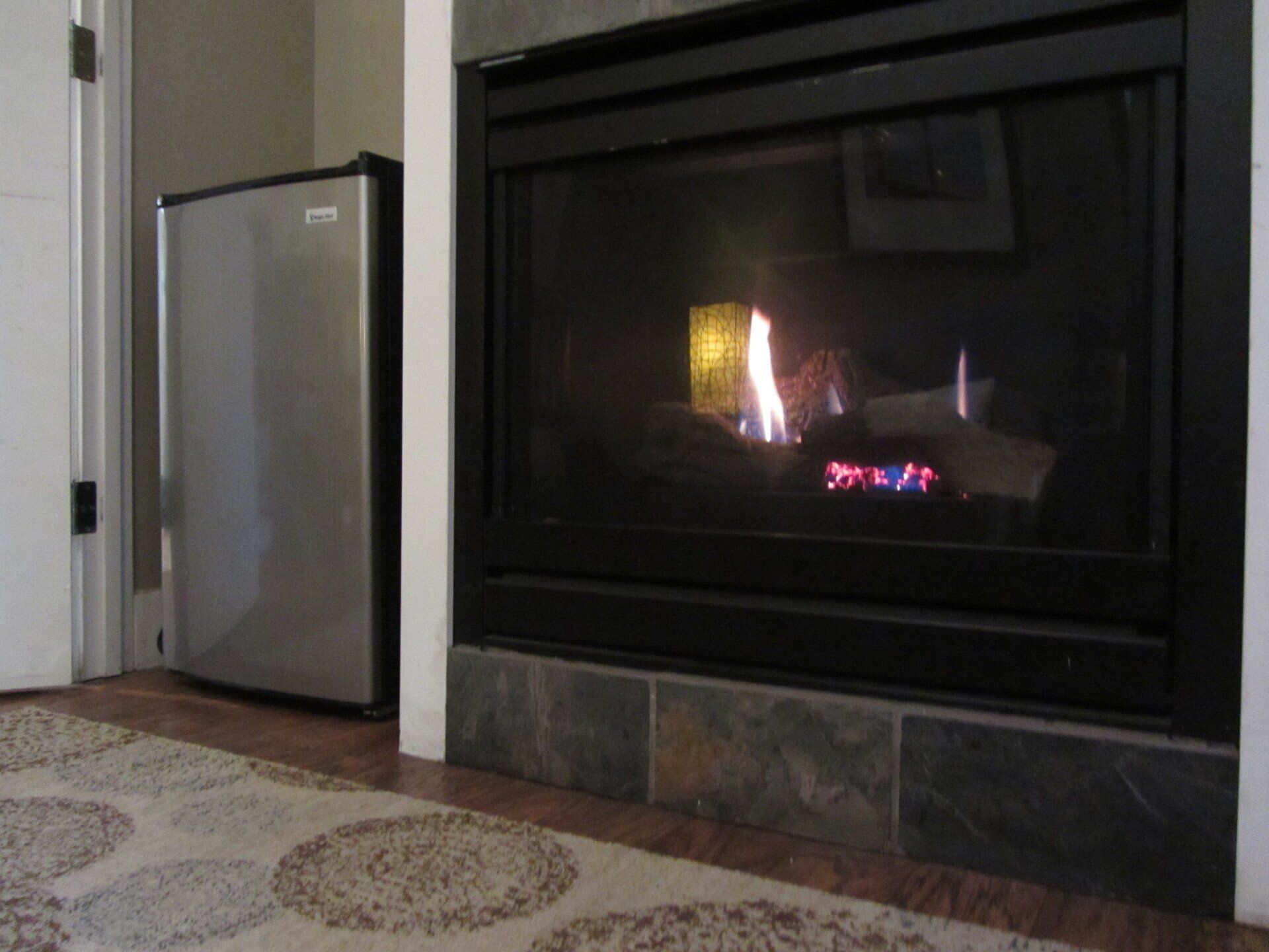 A fireplace with a stainless steel refrigerator in the background