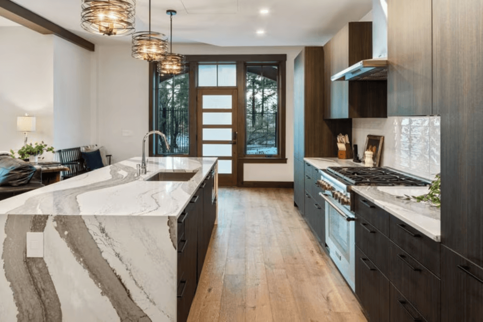 A kitchen with a large island , stainless steel appliances , marble counter tops and wooden floors.