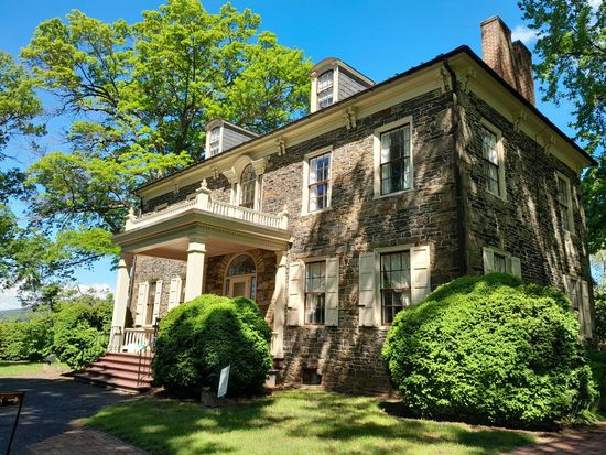 Old stone house with a porch and green bushes under bright blue sky
