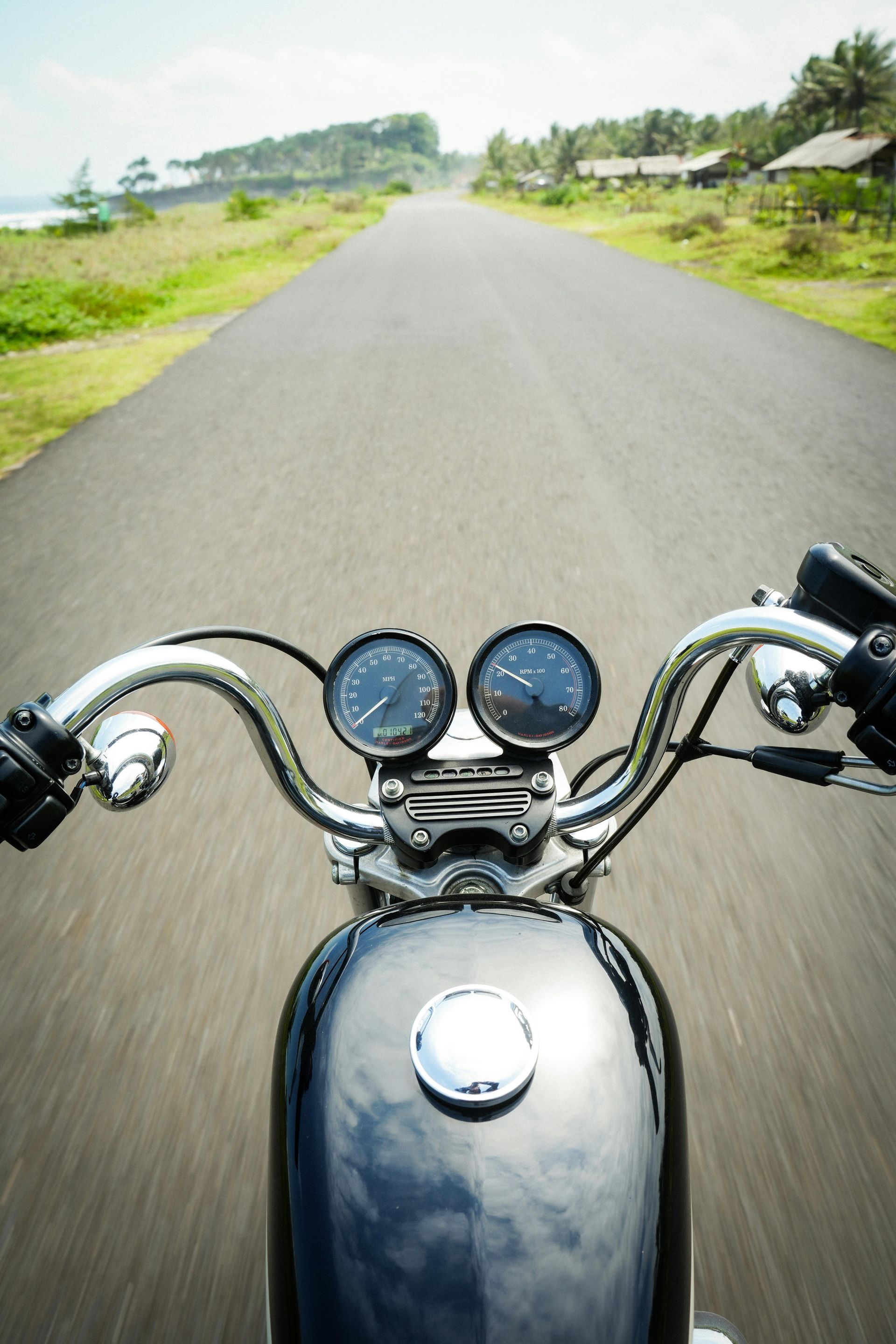 View from a motorcycle on a quiet paved road with green fields on both sides