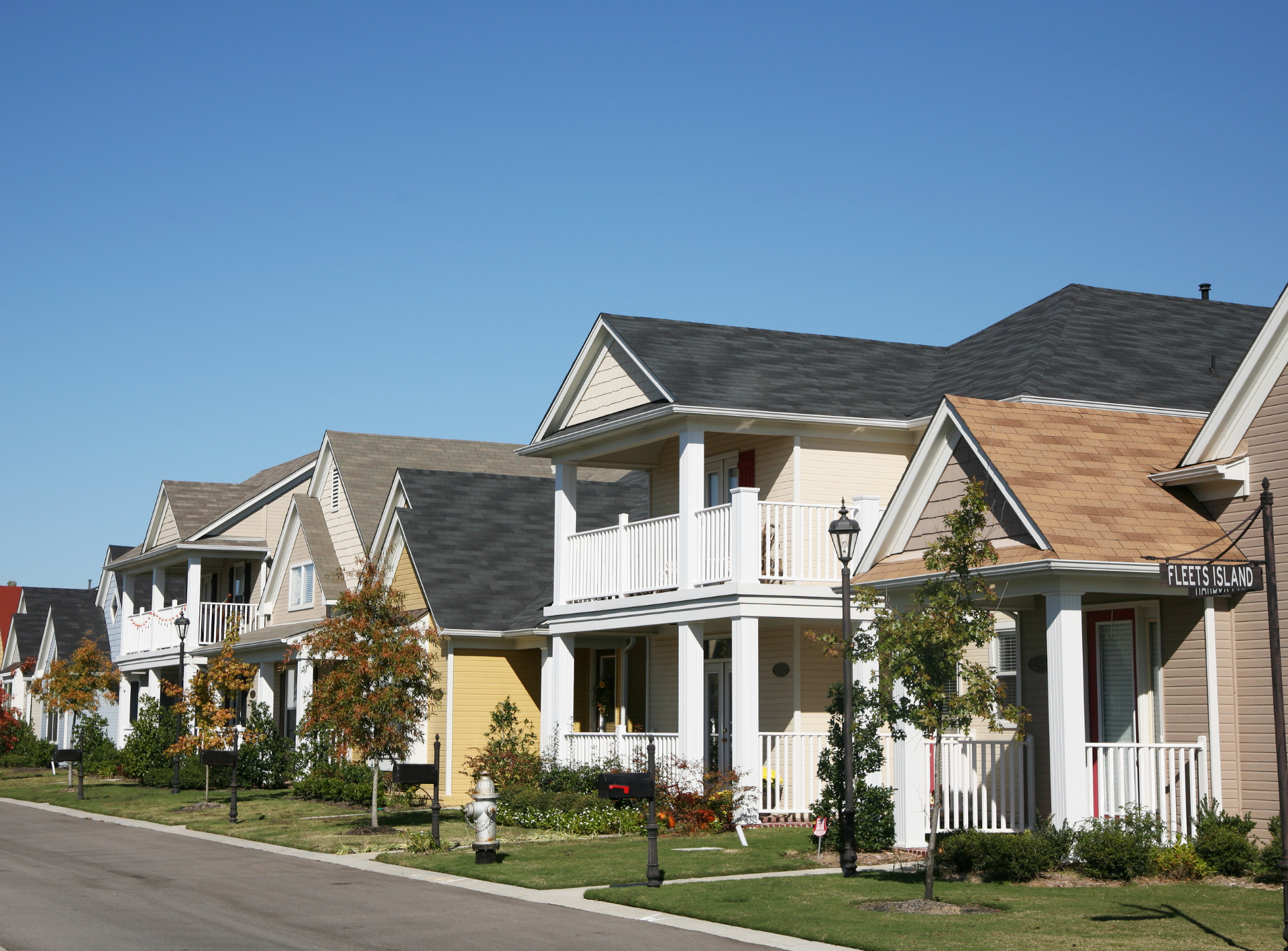 Row of houses with balconies and varying roof colors on a street, under a clear blue sky.