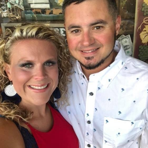 Woman with blonde curly hair and man with dark hair smiling, close together.