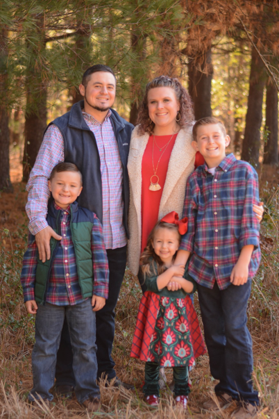 Family of five posing in a forest; smiling, wearing holiday attire.