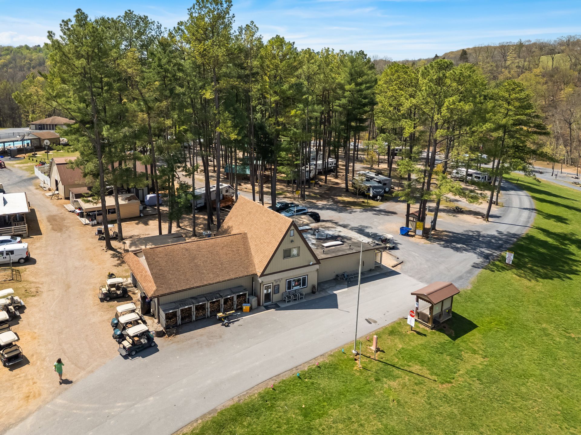 Aerial view of a campground store and office building with parked golf carts, surrounded by trees and RVs on a sunny day.