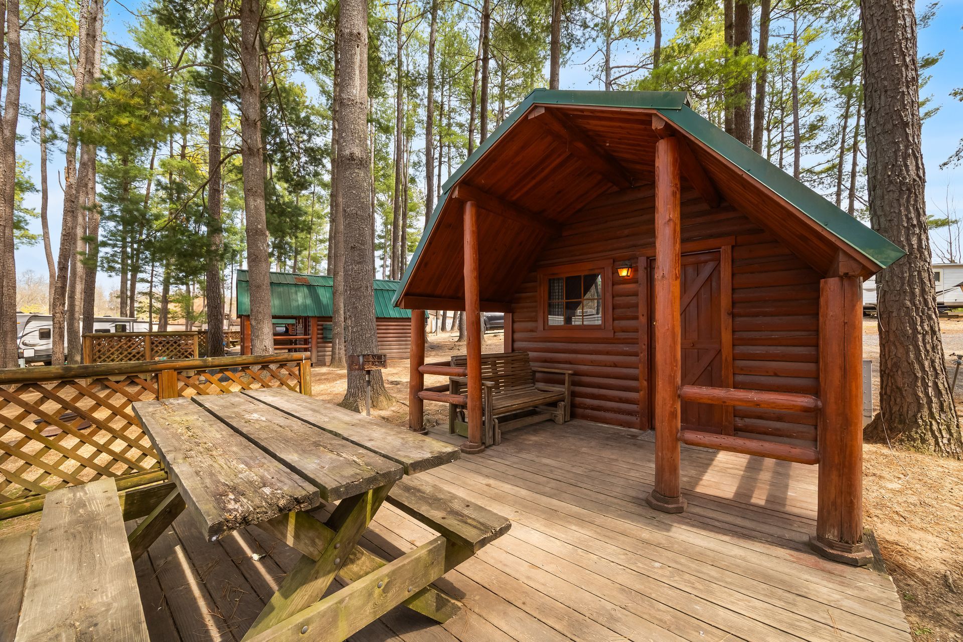 Log camping cabin with a covered porch and picnic table under tall pines
