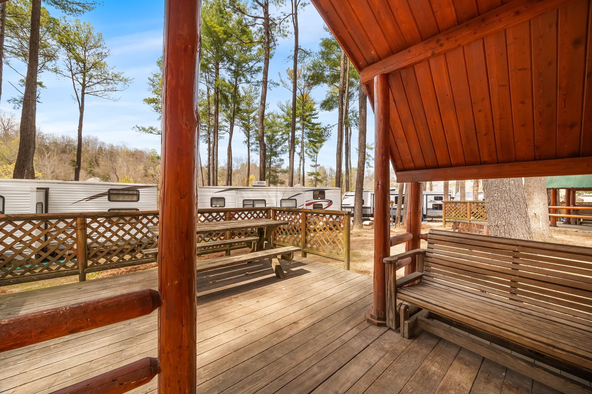 A wooden deck with a bench and a picnic table in the woods.