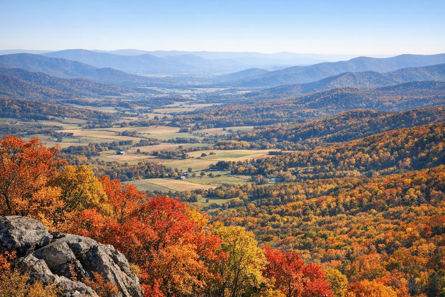 Red, orange and yellow fall trees above Shenandoah Valley farmland with layered Blue Ridge ridgelines