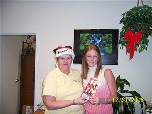 A woman wearing a santa hat is holding a gift for another woman