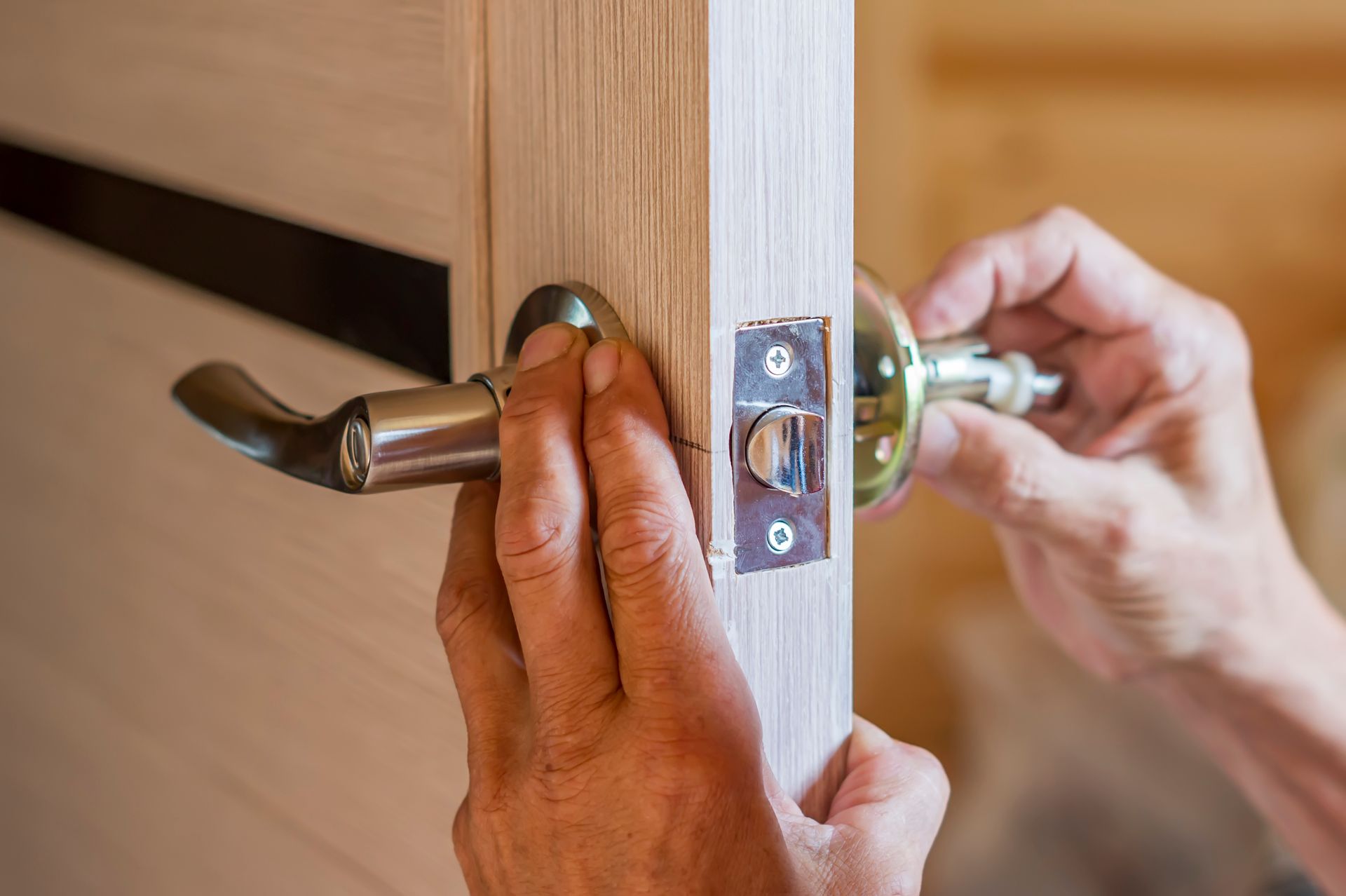 Hands installing a silver door handle on a wooden door.
