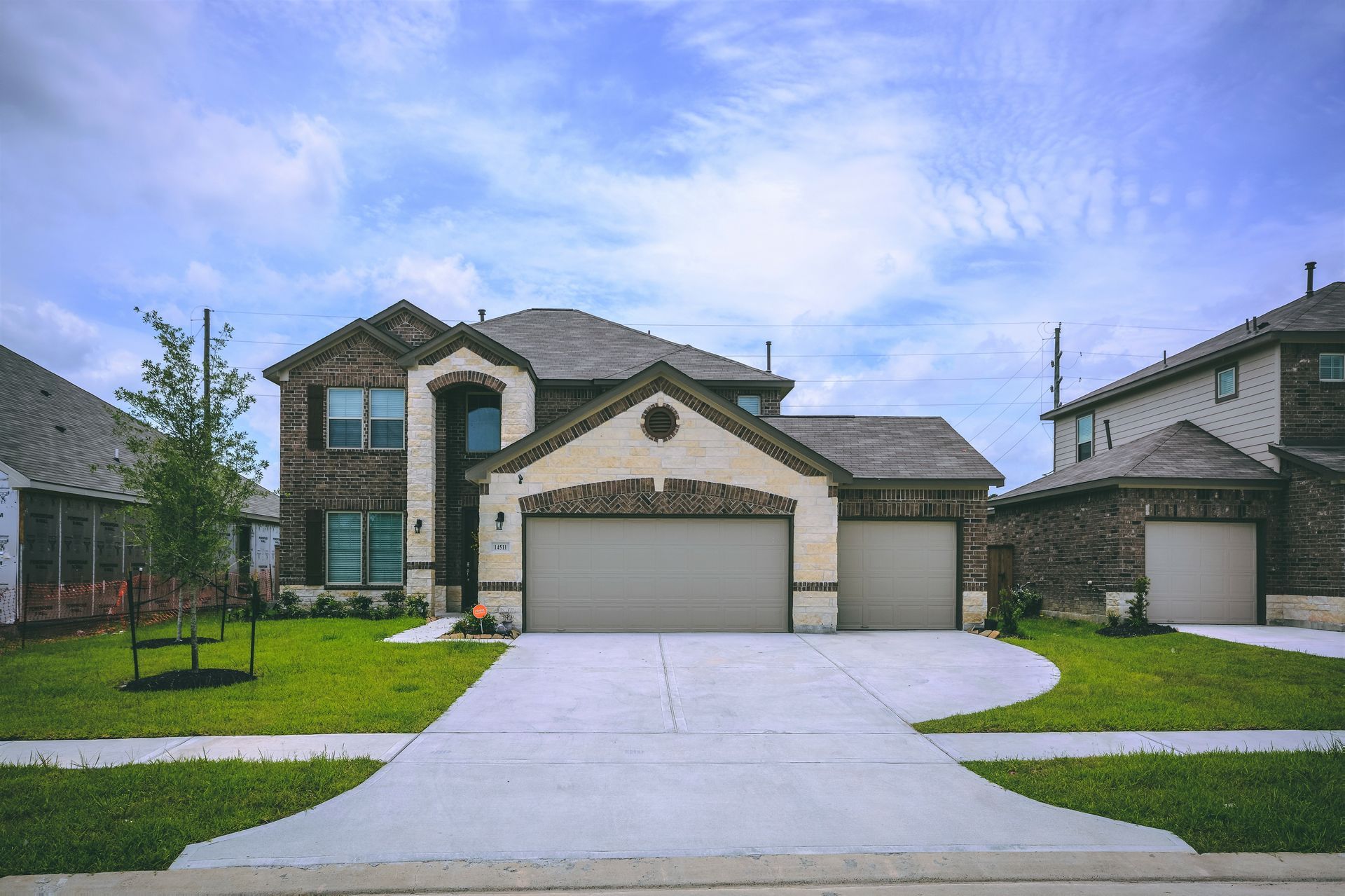 Two-story brick house with attached two-car garage, concrete driveway, and green lawn under a blue sky.