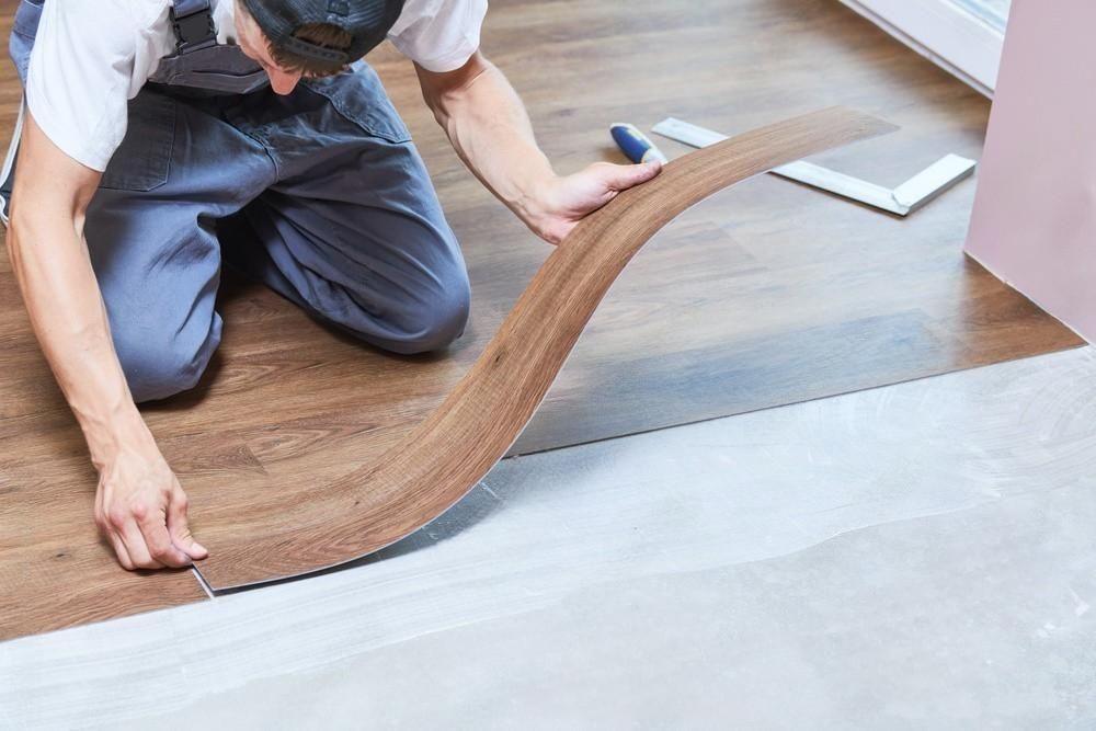 Person installing wood-look vinyl flooring in a room. Kneeling, holding a curved plank, and aligning it with existing flooring.