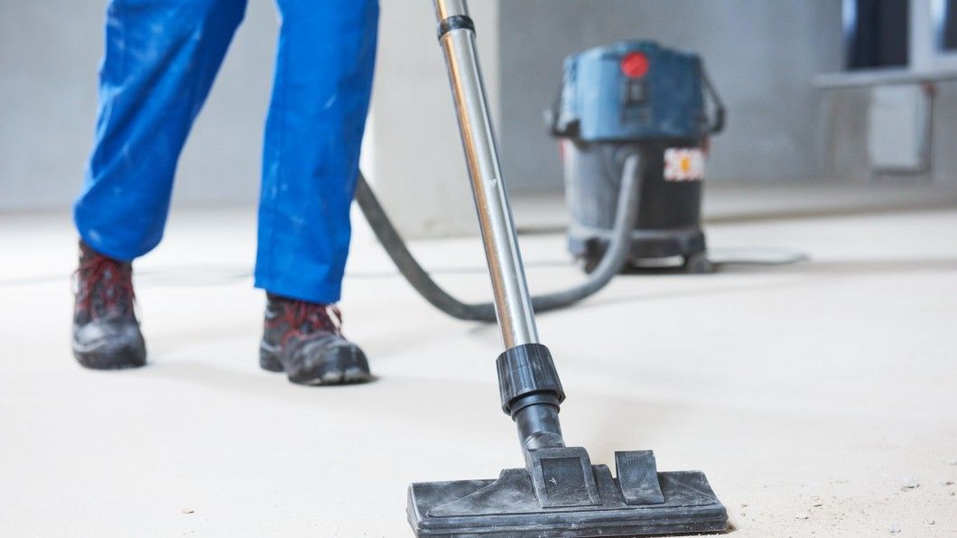 Person in blue overalls vacuuming a dusty floor with a large vacuum cleaner.