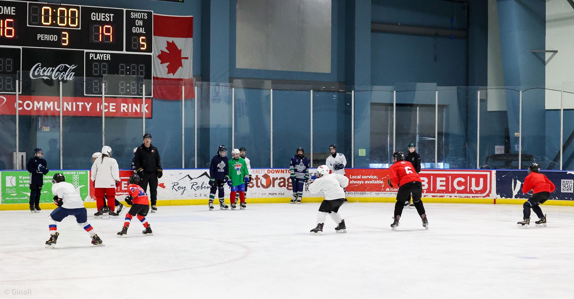 Indoor ice hockey game with players in red, green, and white on the rink near the goal and scoreboard