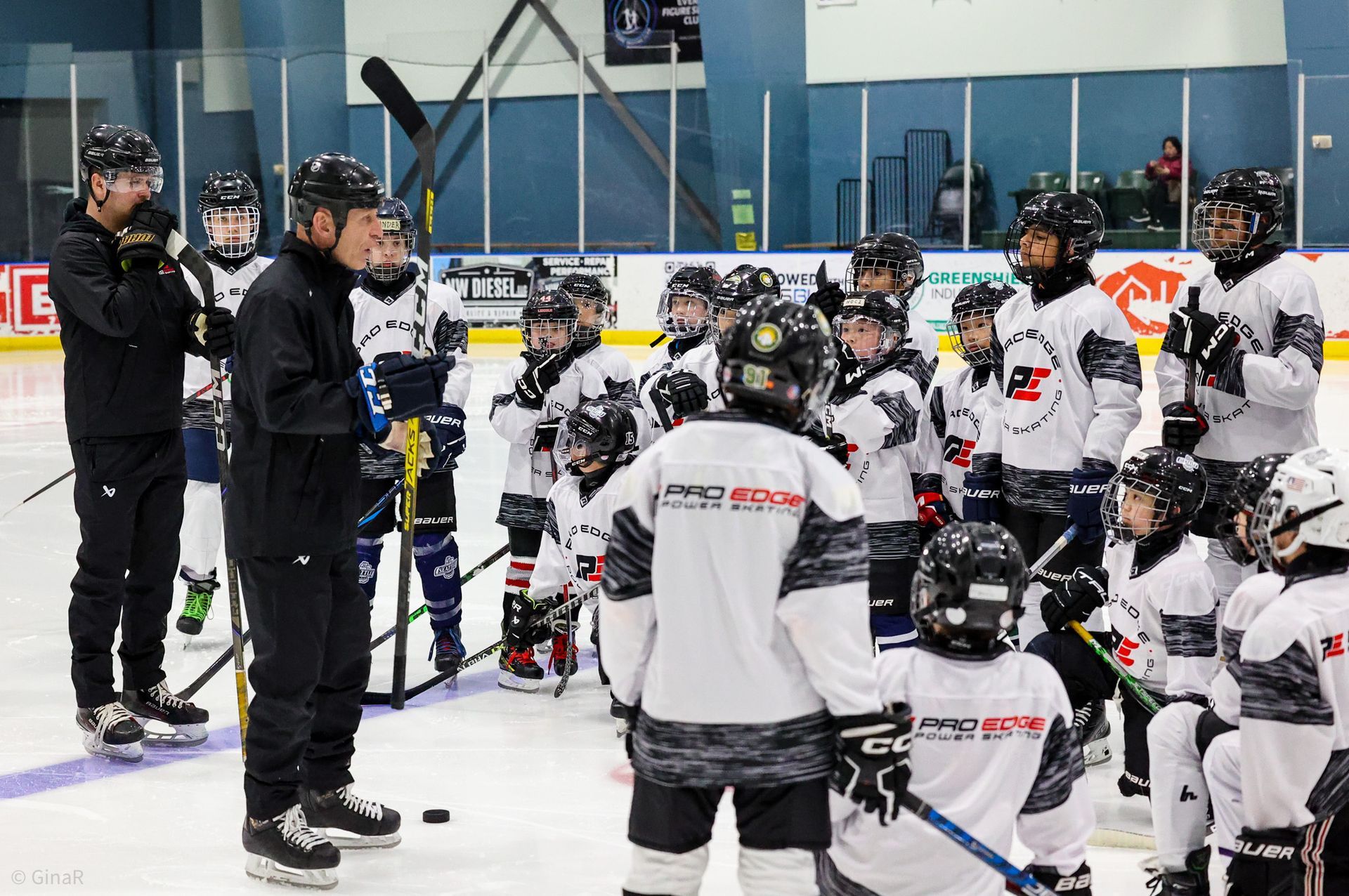 Hockey coach addressing a group of players in white jerseys during an indoor practice session