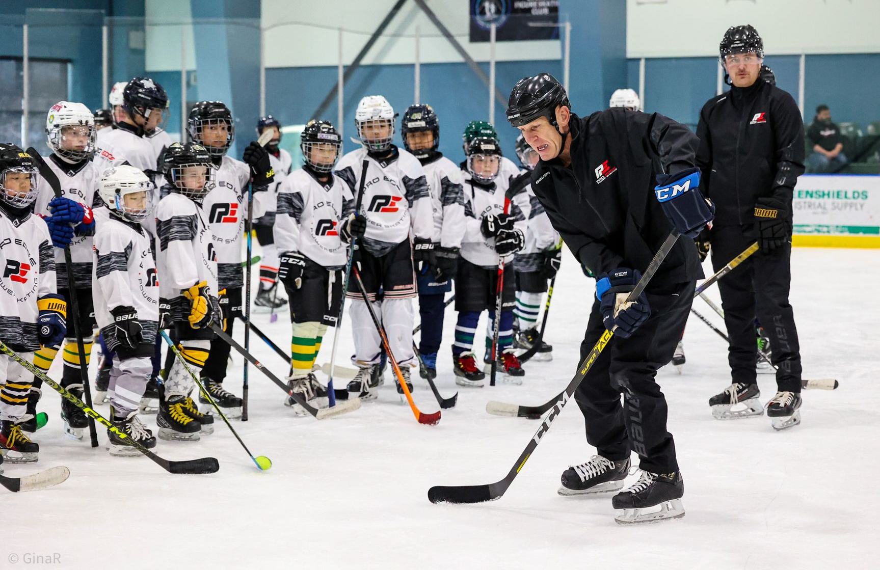 Youth ice hockey players gather on the rink as a coach gives instructions.
