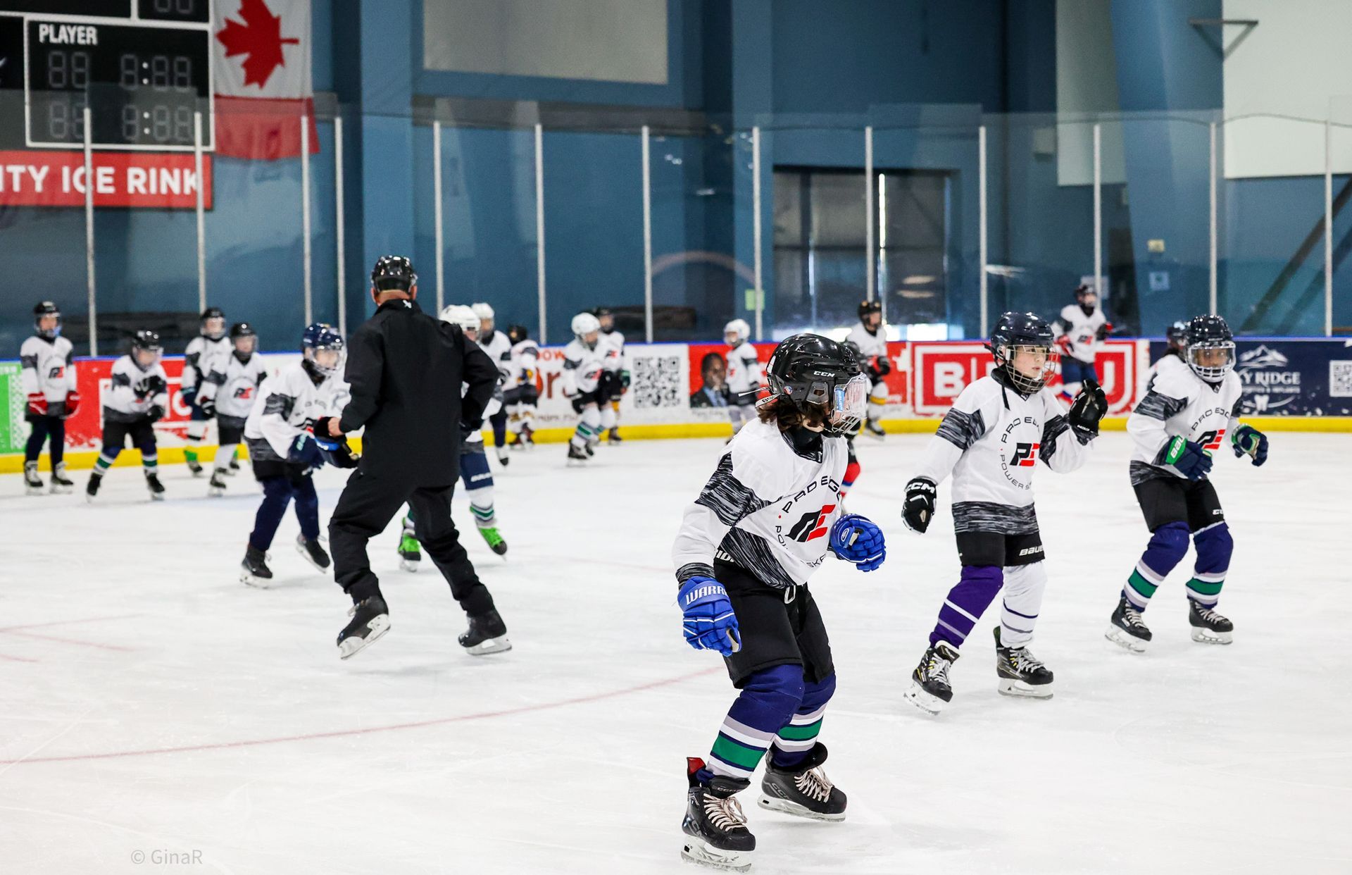 Youth ice hockey game on an indoor rink, players in white and black skating near the boards.