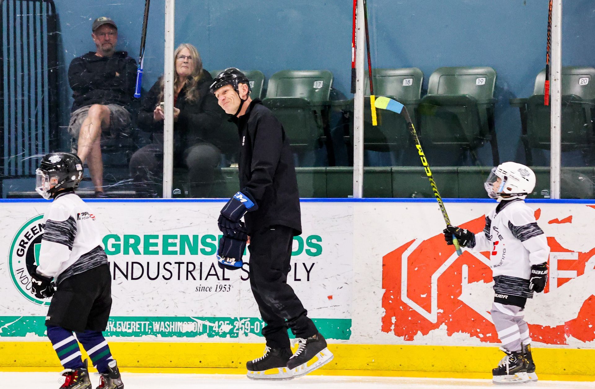 Ice hockey players in white and black jerseys on the rink near the boards and spectators behind glass