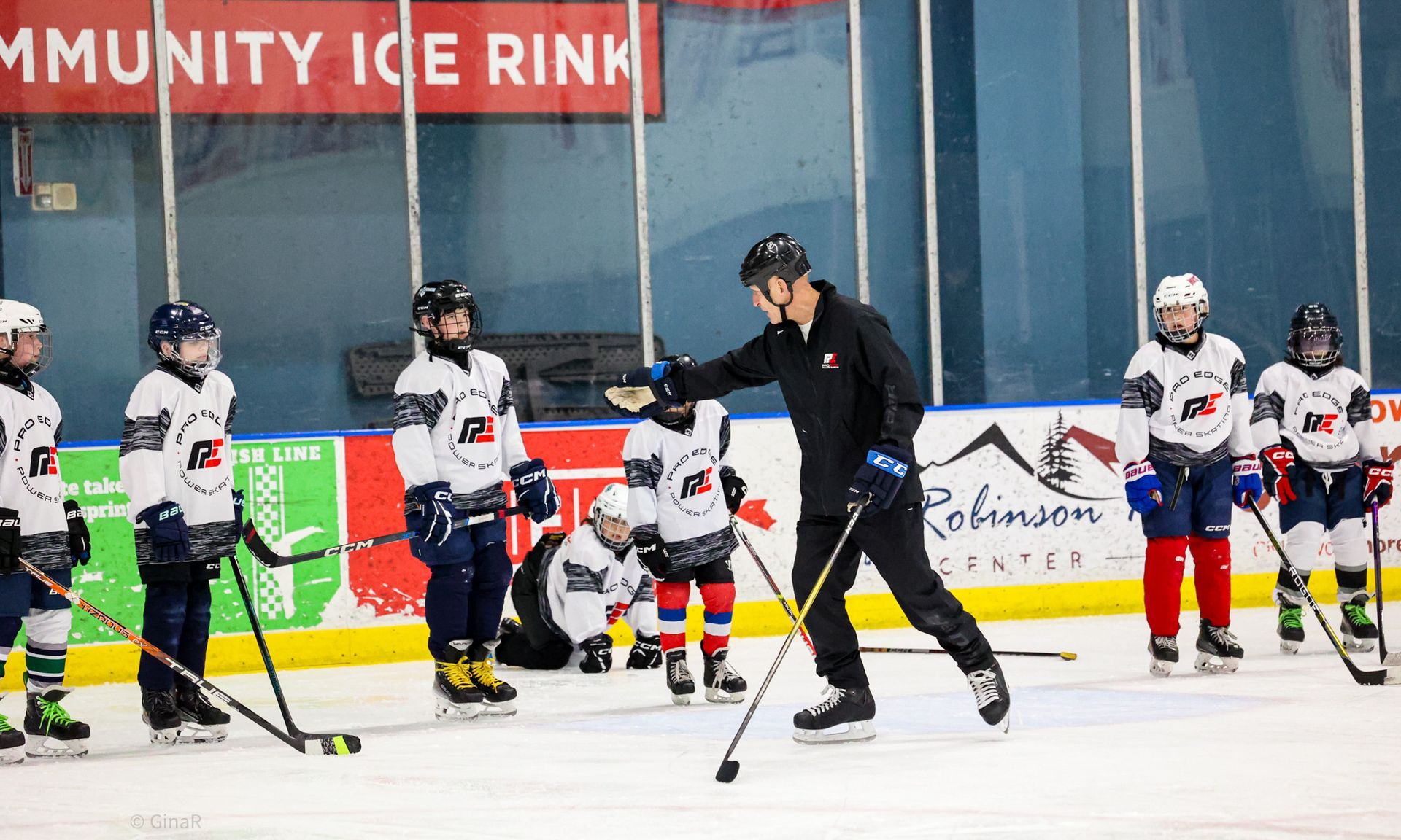 Youth hockey players and coach on indoor ice rink, practicing with sticks and pucks.