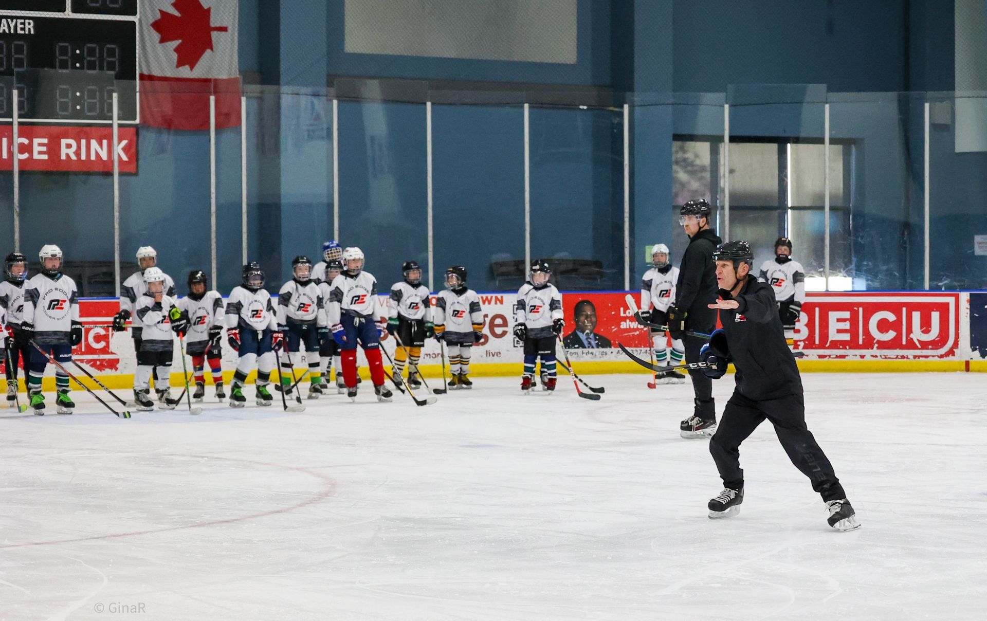 Youth hockey team lined up on ice rink while a skater in black moves in the foreground.