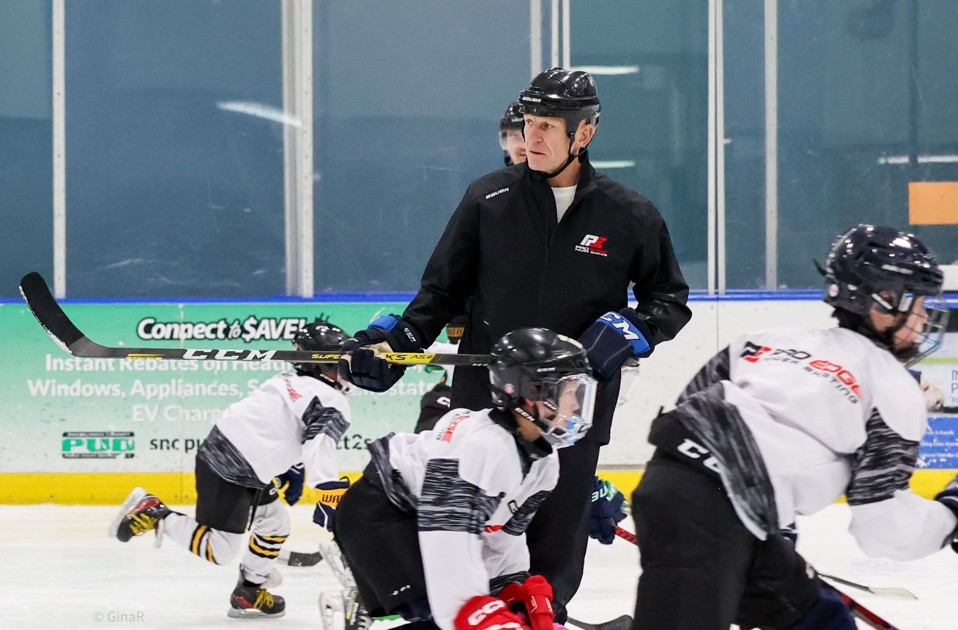 Ice hockey players in white and black gear crouch on the ice while a referee stands behind them near the boards.