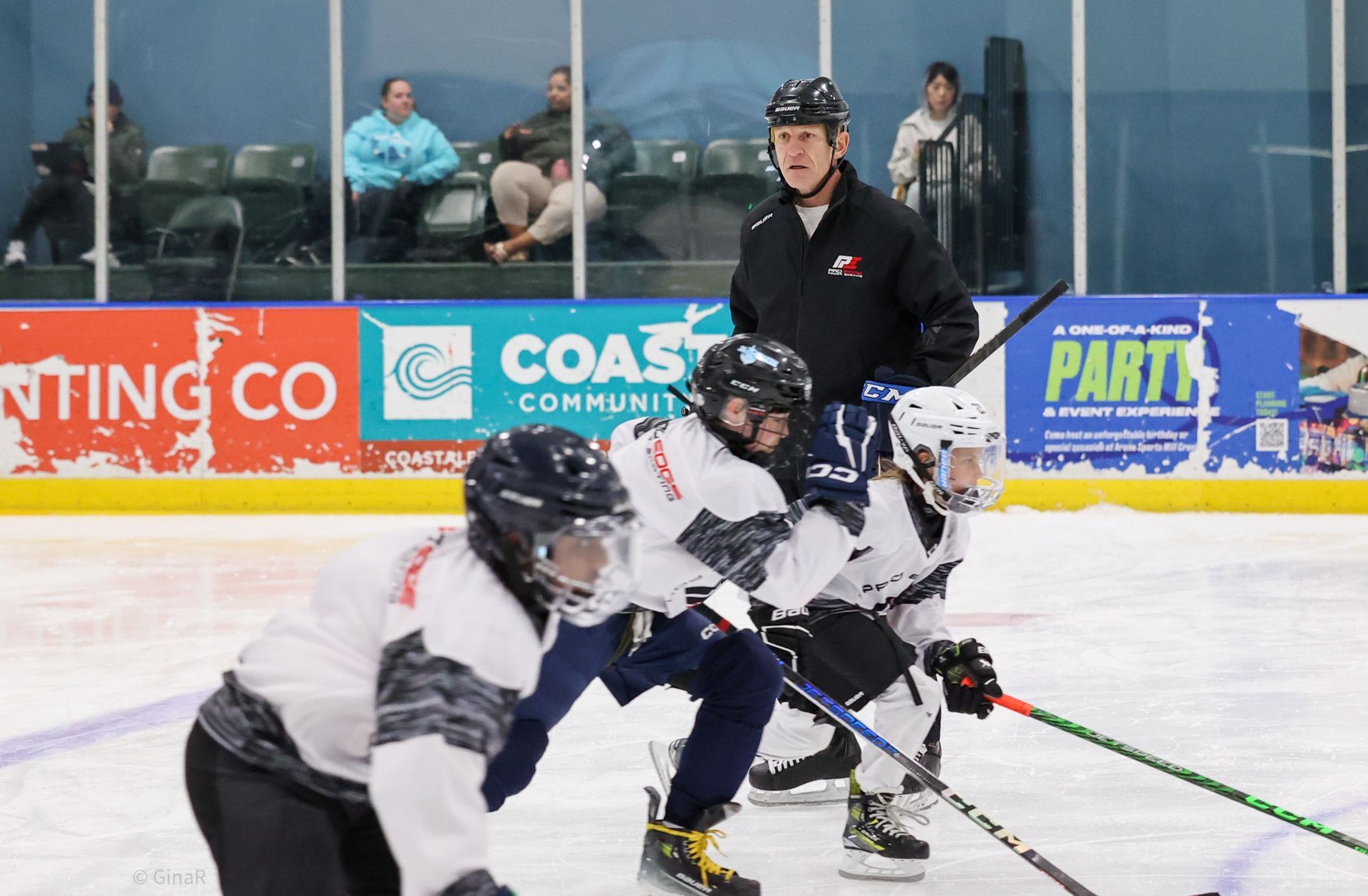 Ice hockey players battling for the puck on an indoor rink, with a referee in the background.