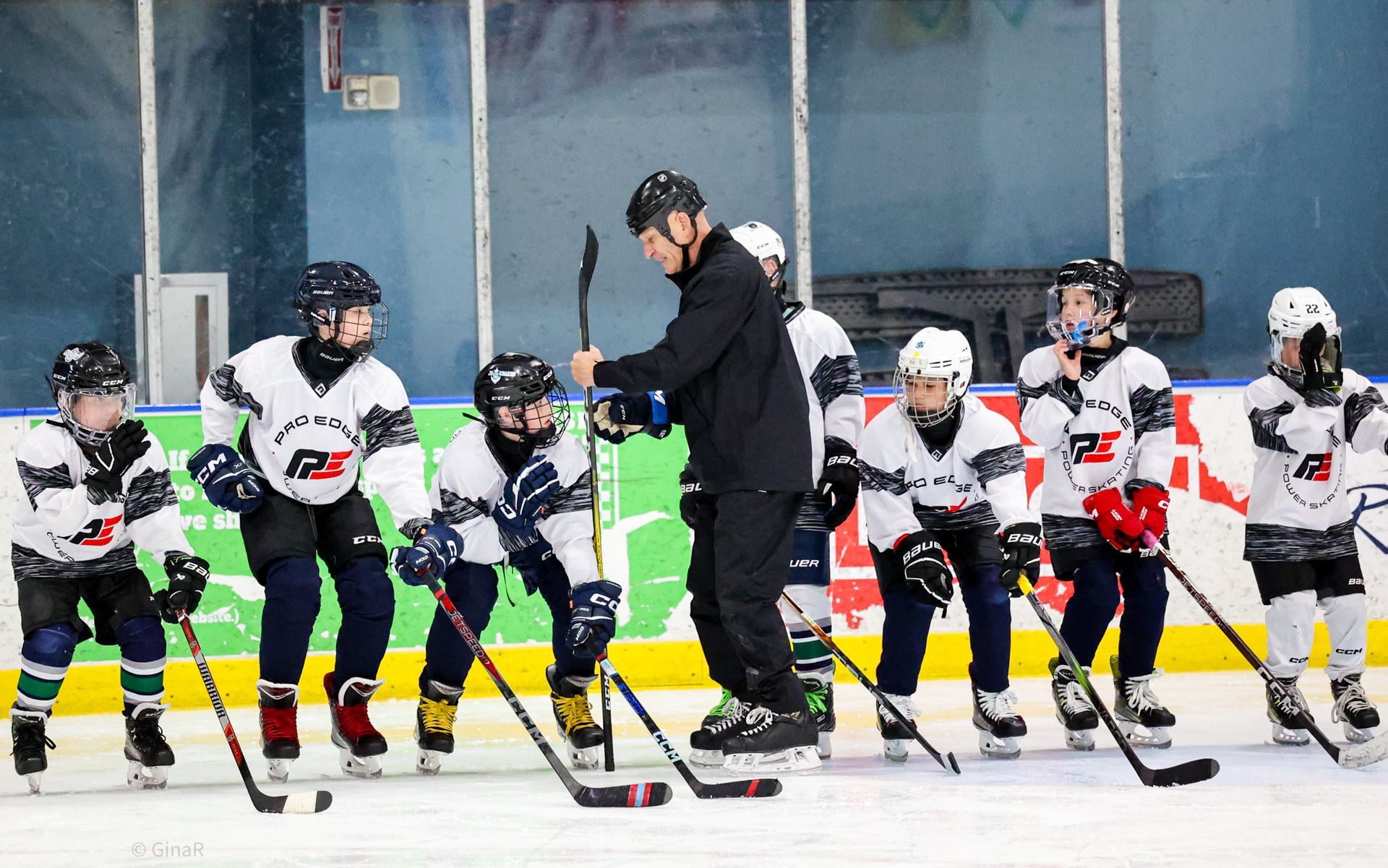 Youth hockey players in white jerseys gather around a coach on an indoor rink