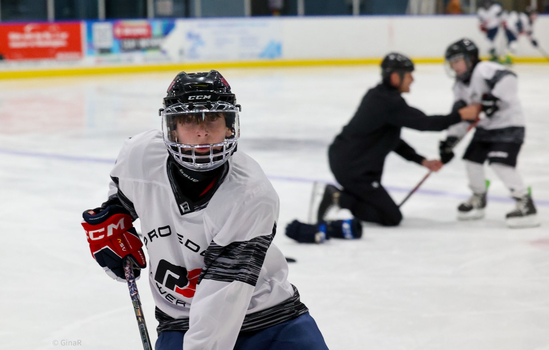 Youth hockey players practice on an ice rink, with one player in white and black in the foreground.