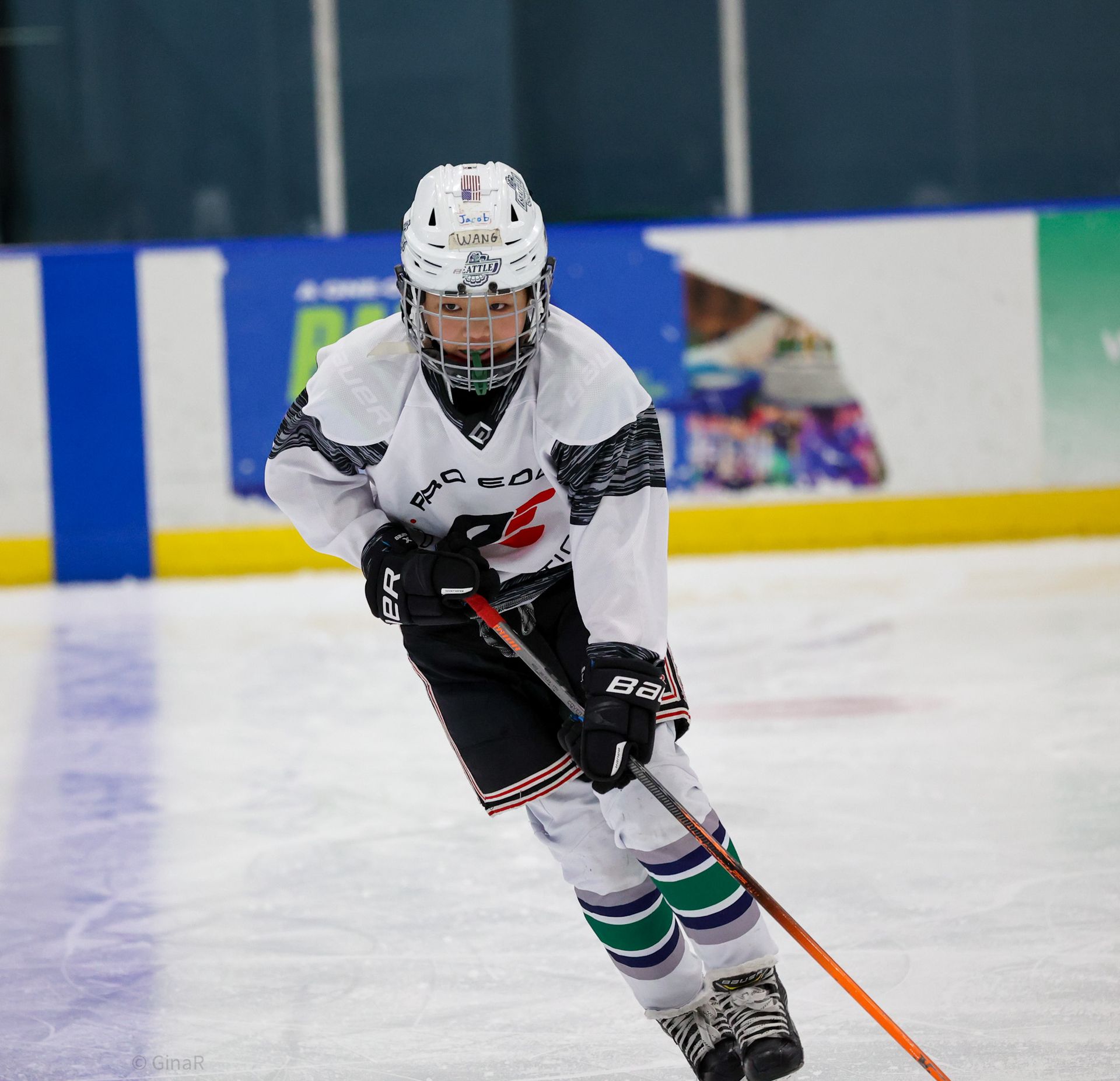 Hockey player in white jersey skating forward on ice, holding a stick with an orange blade
