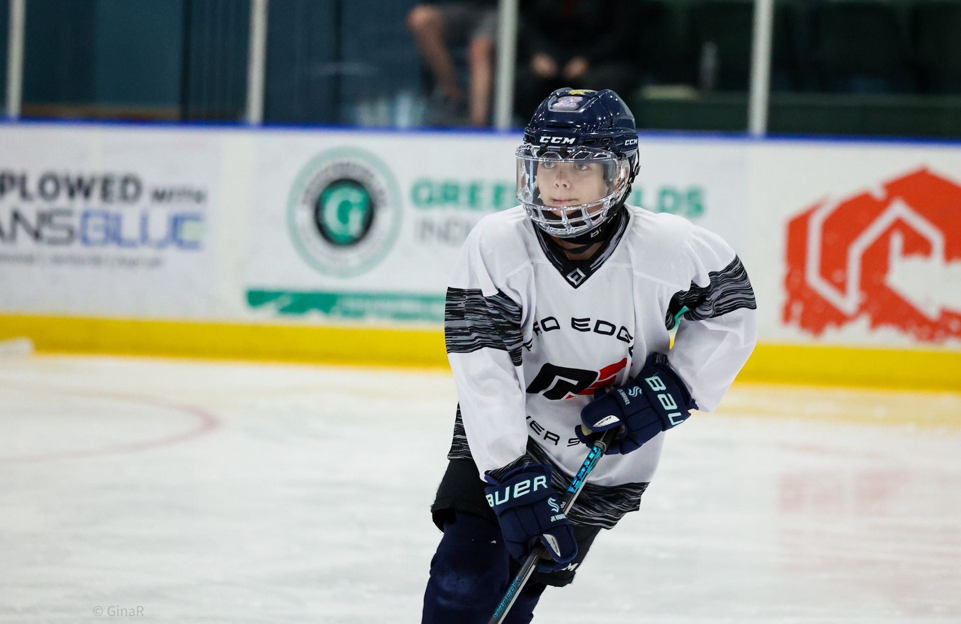 Ice hockey player in white and navy uniform skating on the rink with stick in hand