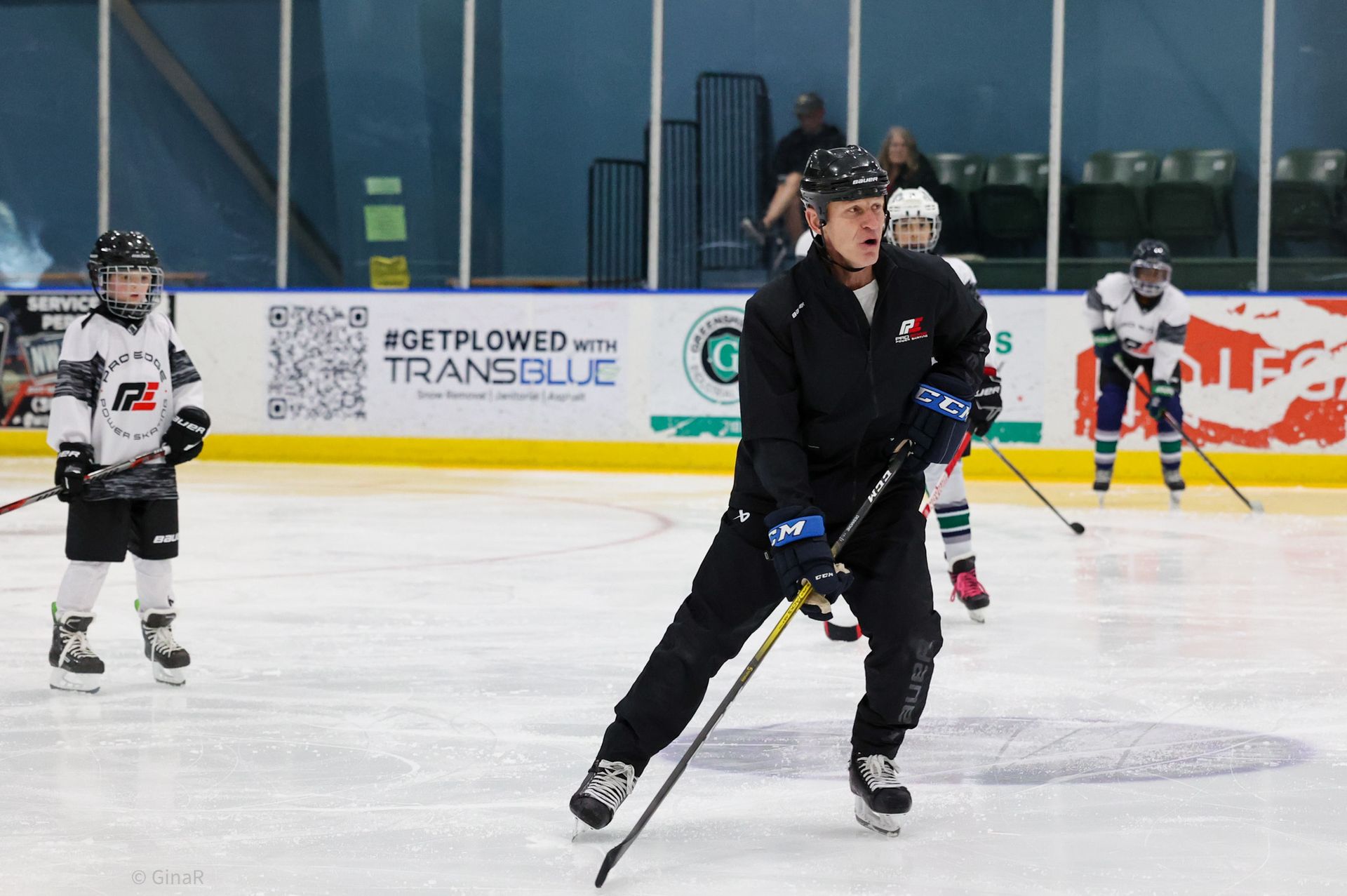Hockey players on an indoor ice rink, one in black skating forward with a stick.