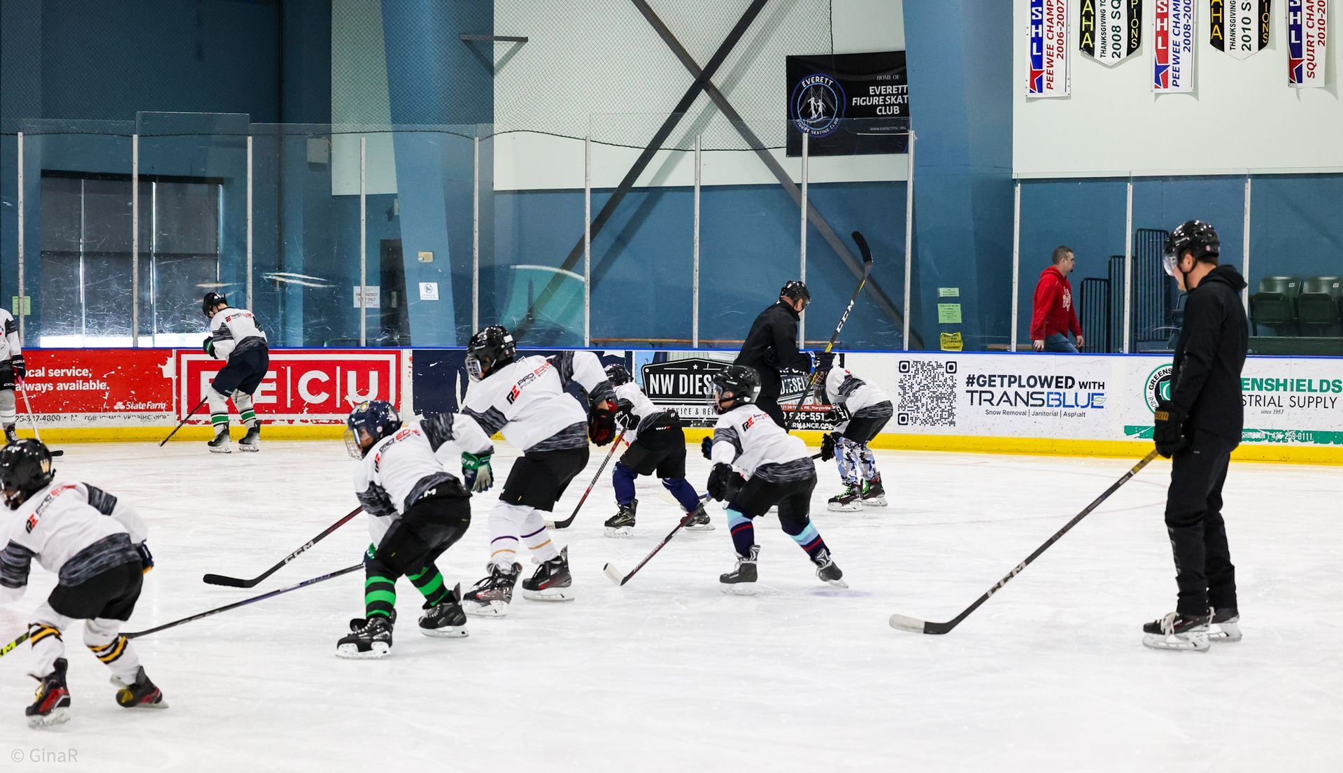 Hockey players in black and white jerseys face off on an indoor ice rink, with a referee nearby.
