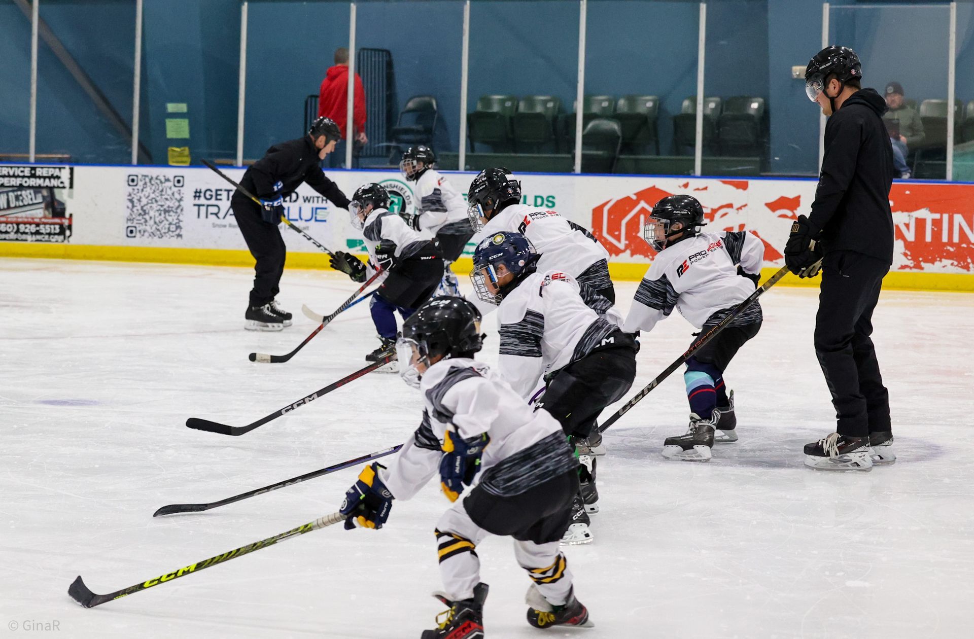 Youth hockey players skating on ice during practice, with a coach standing nearby.